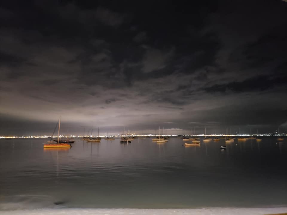 Boats sit at anchor in a bay with large, dark clouds in the sky.